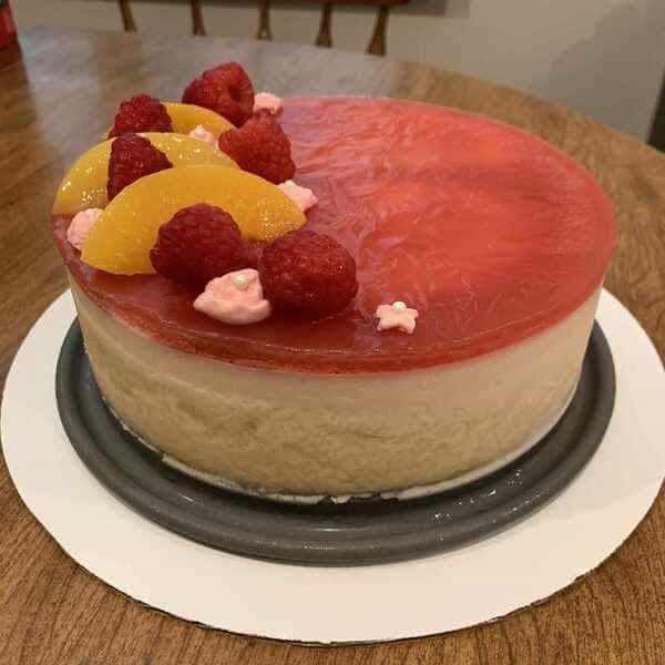 This image shows a layered cake with the top layer being raspberry gelatin. It is topped with sliced 
        peaches and raspberry.